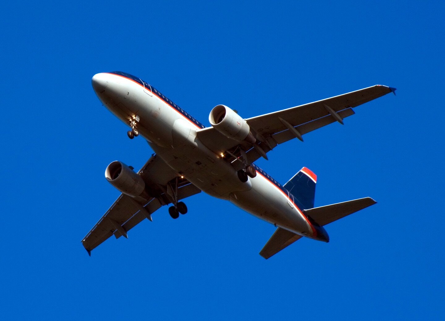 Ilustracja przedstawia lecący biało-granatowy samolot z czerwonymi elementami. Samolot ma opływowy kształt.