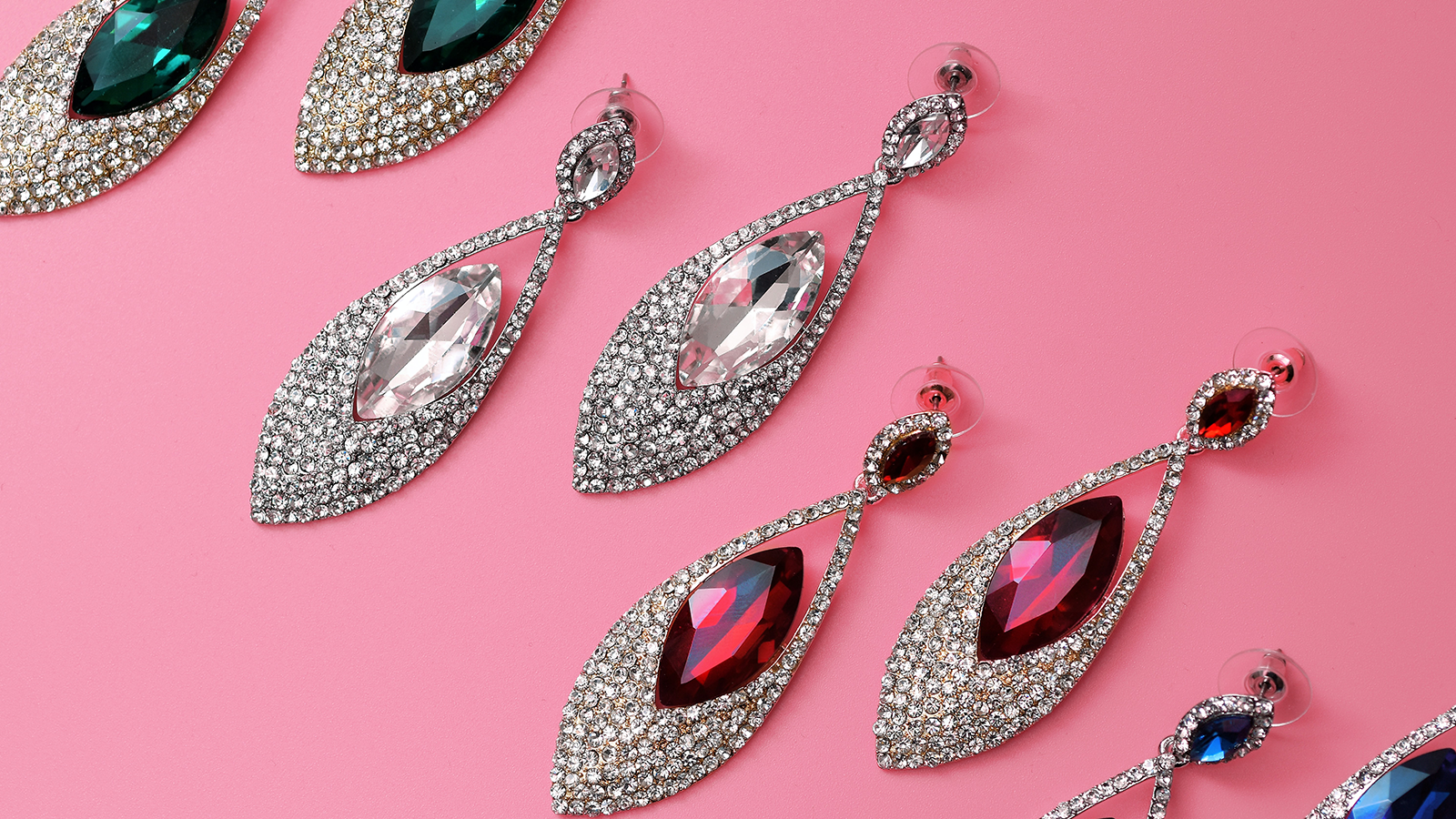 Zdjęcie przedstawia kilka par kolczyków w kształcie łezki wysadzanej dookoła diamentami oraz kamieniem szlachetnym pośrodku. Każda para kolczyków ma kamienień w innym kolorze. 