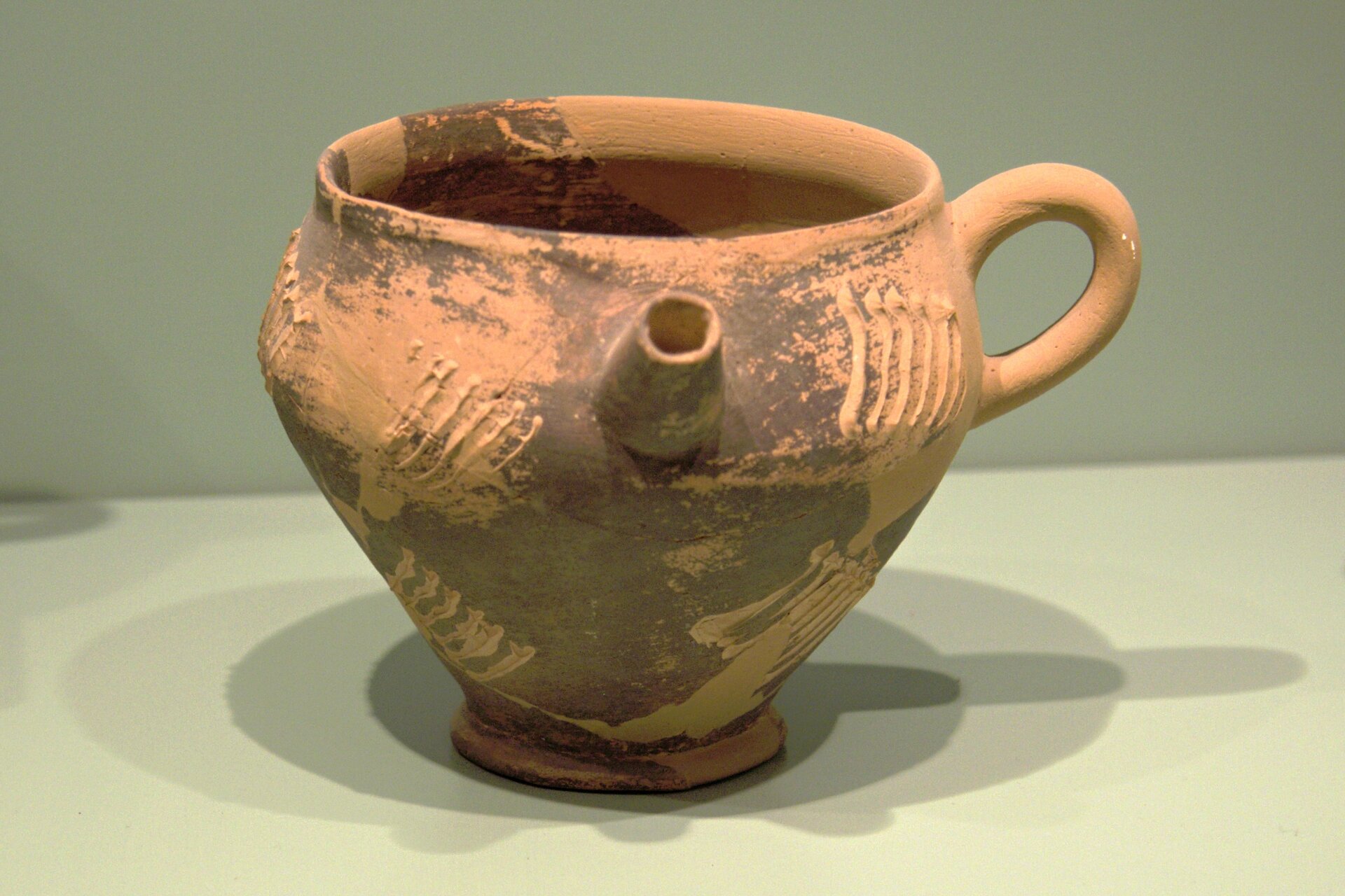 Fotografia autorstwa Zdenka Kratochvila przedstawia starożytną wazę glinianą pochodzącą z Krety. Naczynie swoim kształtem przypomina imbryczek lub czajniczek, i zostało wykonane z jasnej gliny; posiada dziubek po przekątnej ucha. Fotografia wazy została wykonana na tle szarej ściany.