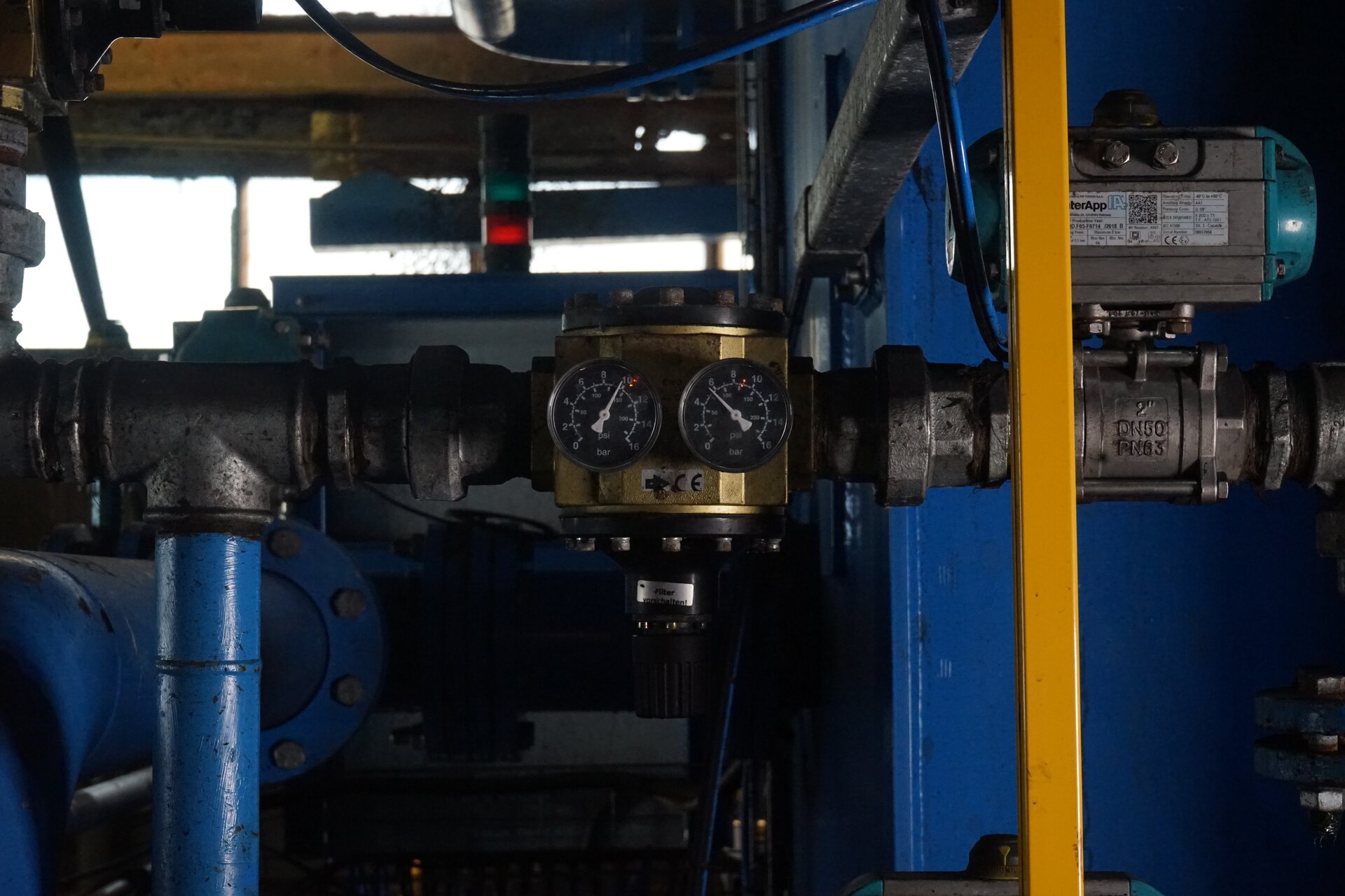 Zdjęcie przedstawia pompę próżniową wraz z manometrami. Pompa zabudowana jest z lewej strony i ma cylindryczny kształt. z prawej strony za pomocą pierścieni i rur połączona jest z manometrami oraz resztą układu, w którym generowane jest zmniejszone ciśnienie. Wartości ciśnienia rejestrowanego przez manometry pokazują wskazówki zamontowane na tarczach. Poniżej zdjęcia znajduje się przycisk multimedialny z nagraniem audio. Treść nagrania jest zgodna z tytułem zdjęcia.