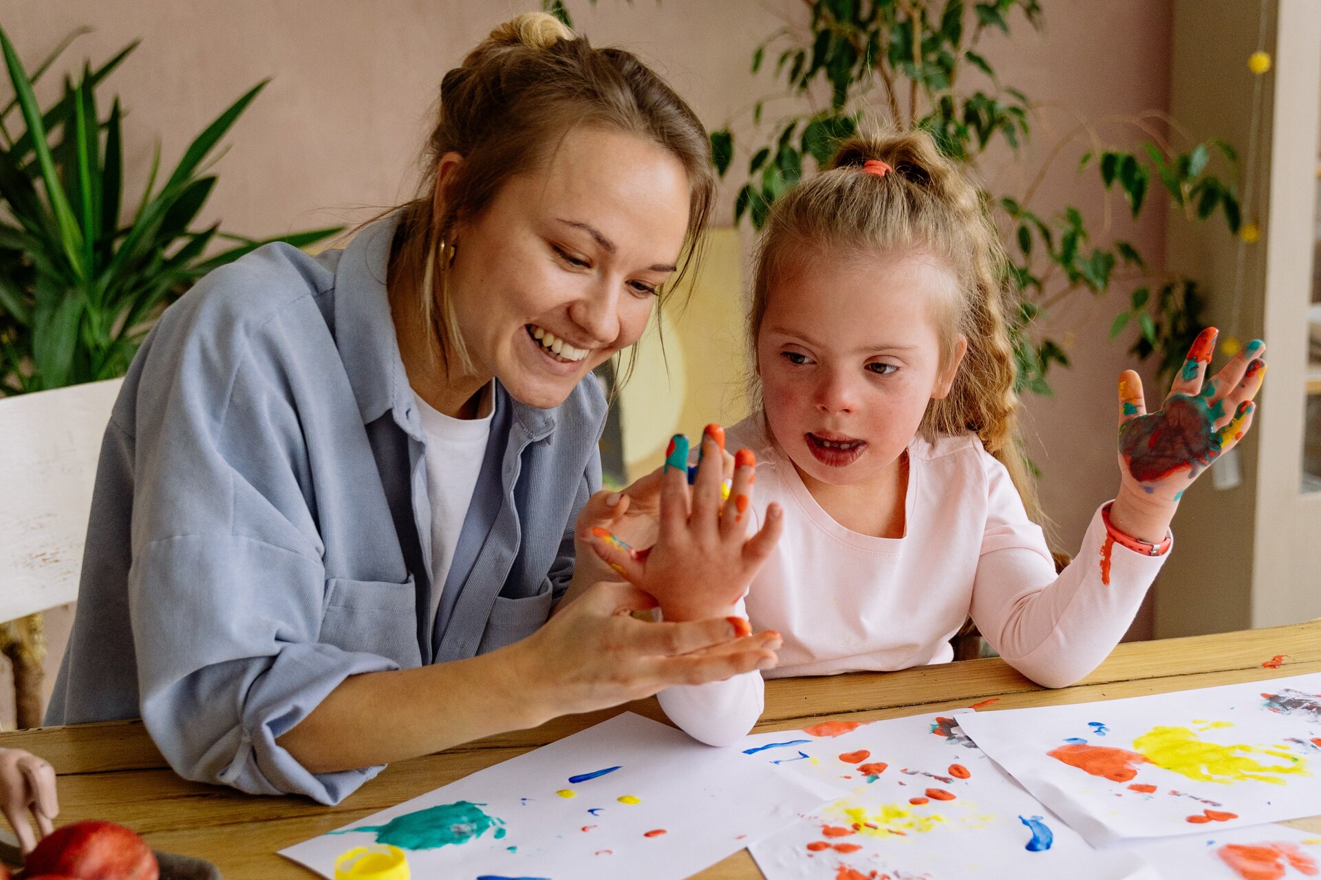 Obraz przedstawia kobietę i dziewczynkę, które malują farbami. Dziewczynka ma pobrudzone farbami dłonie.