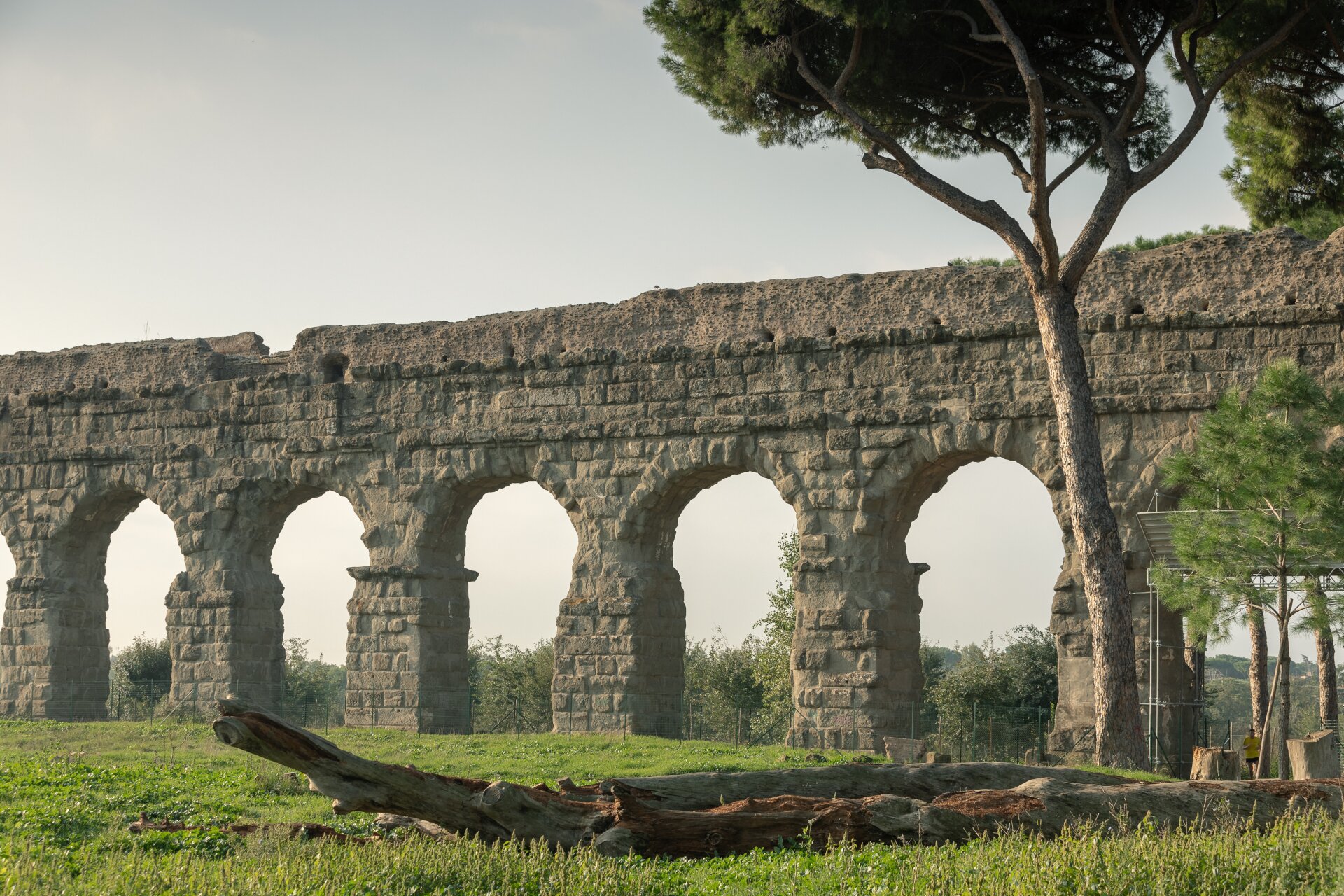 Fotografia przedstawia fragment starożytnego akweduktu zbudowanego z jasnych kamieni. Akwedukt biegnie po równinie porośniętej trawą.