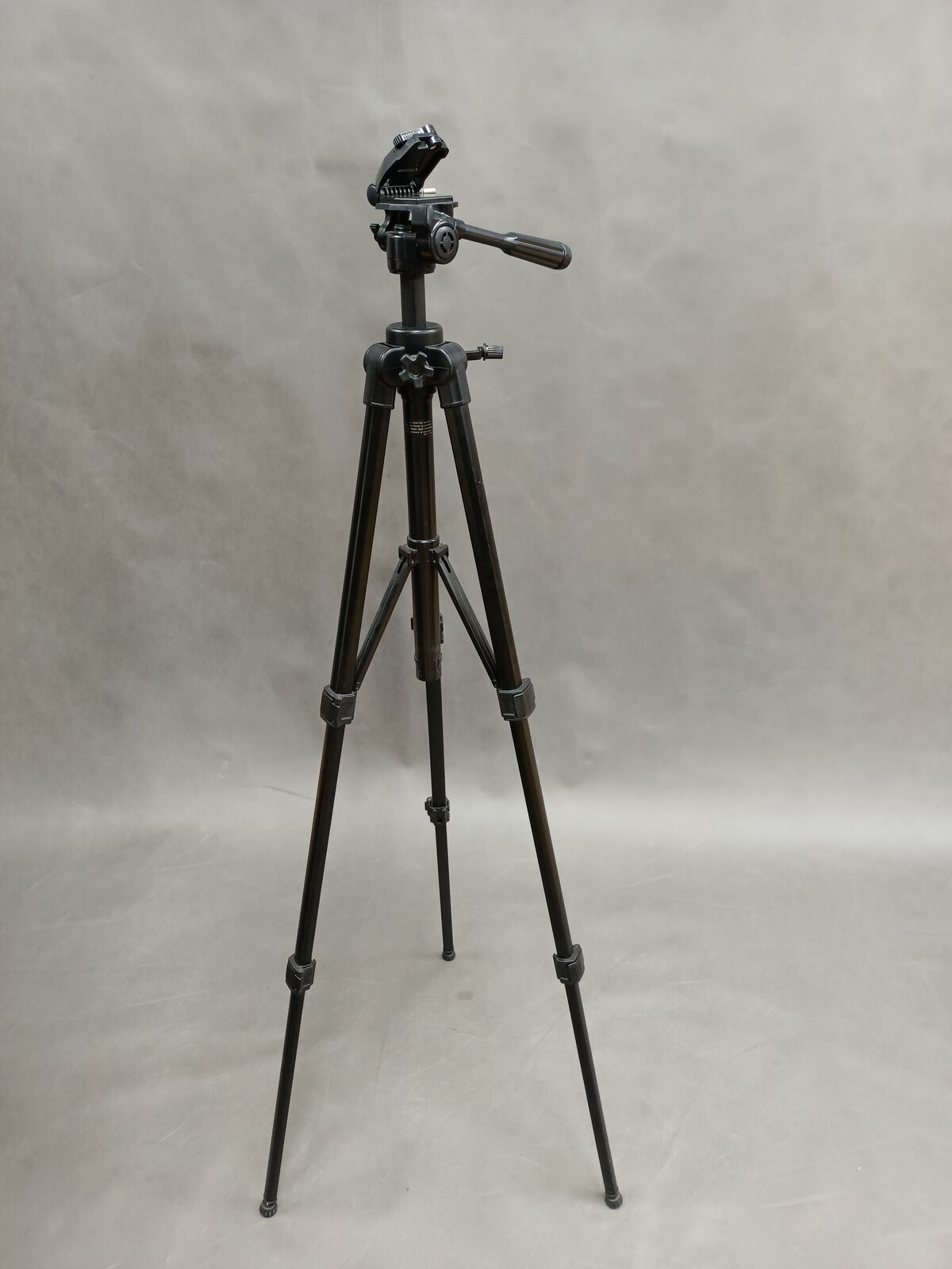 Zdjęcie przedstawia przykładowy statyw z rozstawionymi trzema nogami oraz głowicą znajdującą się w jego górnej części, do której mocuje się na przykład aparat fotograficzny.