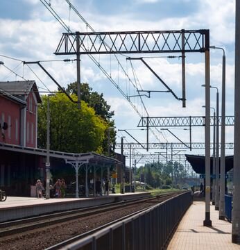 Zdjęcie przedstawia konstrukcję z wysięgiem przez dwa tory. Widoczny jest tor kolejowy, który rozdziela się na dwa tory. Wzdłuż torów stoją podpory. Na pojedynczych podporach zamontowane są poprzecznie dźwigary.