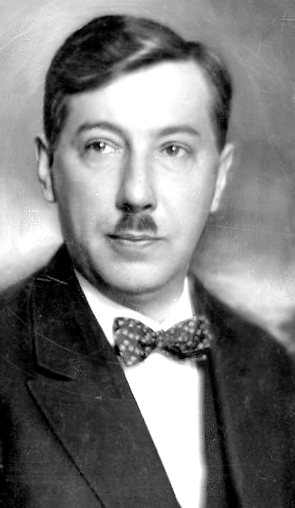 Fotografia przedstawia mężczyznę o ciemnych włosach zaczesanych na lewą stronę. Posiada wąsik i ciemne oczy. Ubrany jest w marynarkę, białą koszulę oraz muszkę. Zdjęcie jest czarno‑białe.