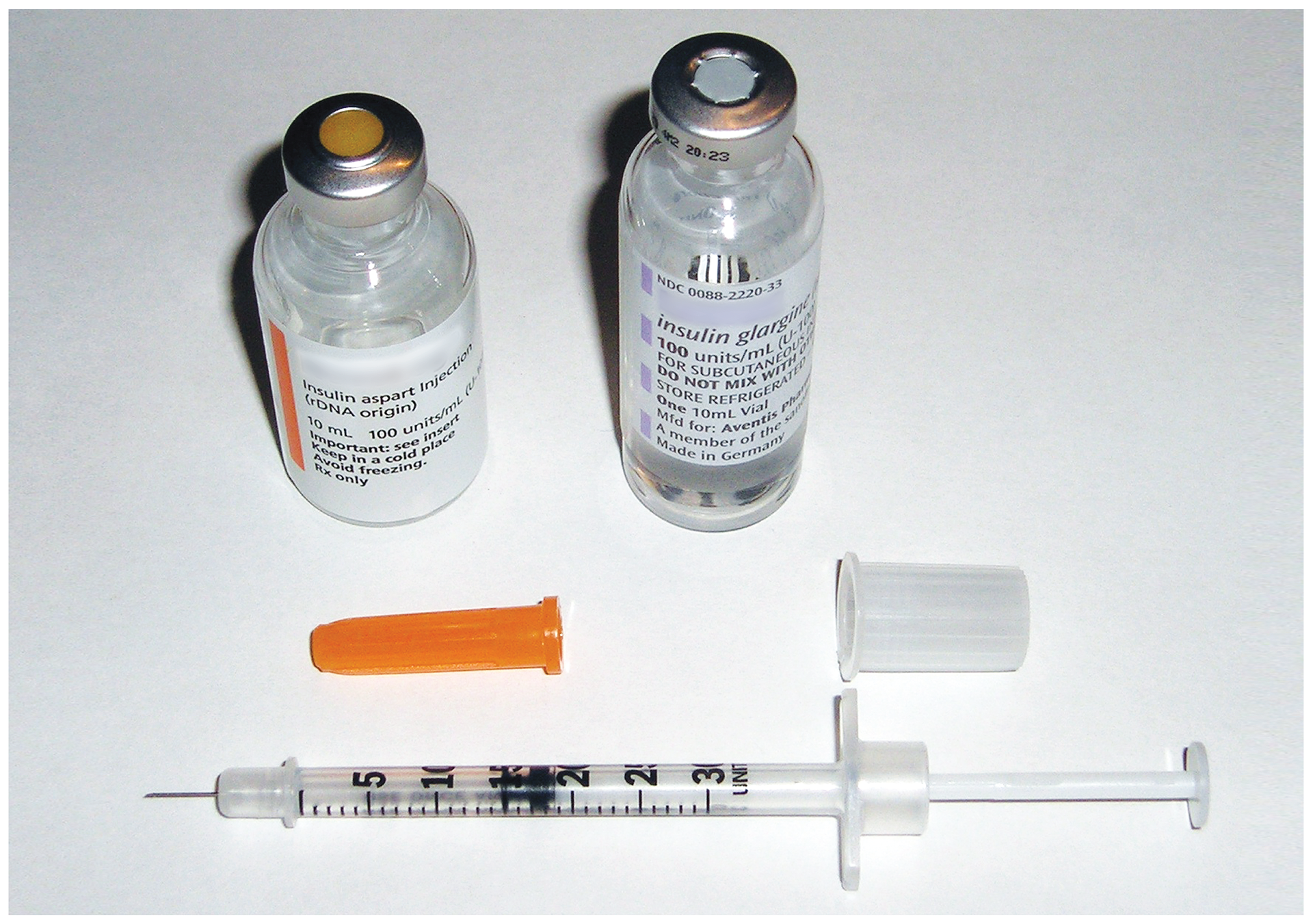 Fotografia przedstawia dwie buteleczki medyczne. Pod nimi leży pomarańczowa osłonka igły, plastikowy kapturek i wąska strzykawka z krótką igłą. Bakterie służą do produkcji szczepionek i leków.