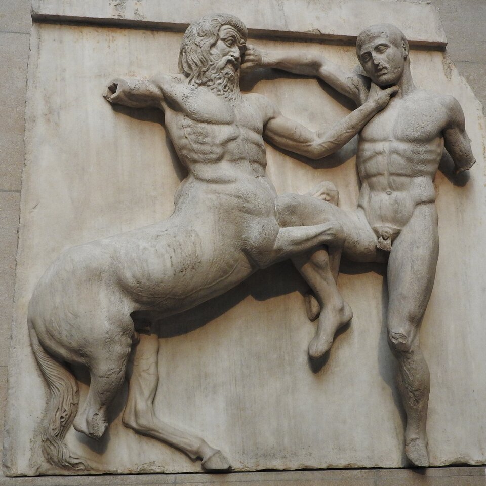 Ilustracja przedstawia metopę ukazującą centaura atakującego Lapita. Na zdjęciu widnieje płaskorzeźba ze sceną walki nagiego wojownika z centaurem. Autor z dużą dbałością wymodelował muskulaturę postaci. Płaskorzeźba jest niekompletna. Postaci mężczyzny brakuje lewej a centaurowi prawej ręki oraz prawego kopyta.