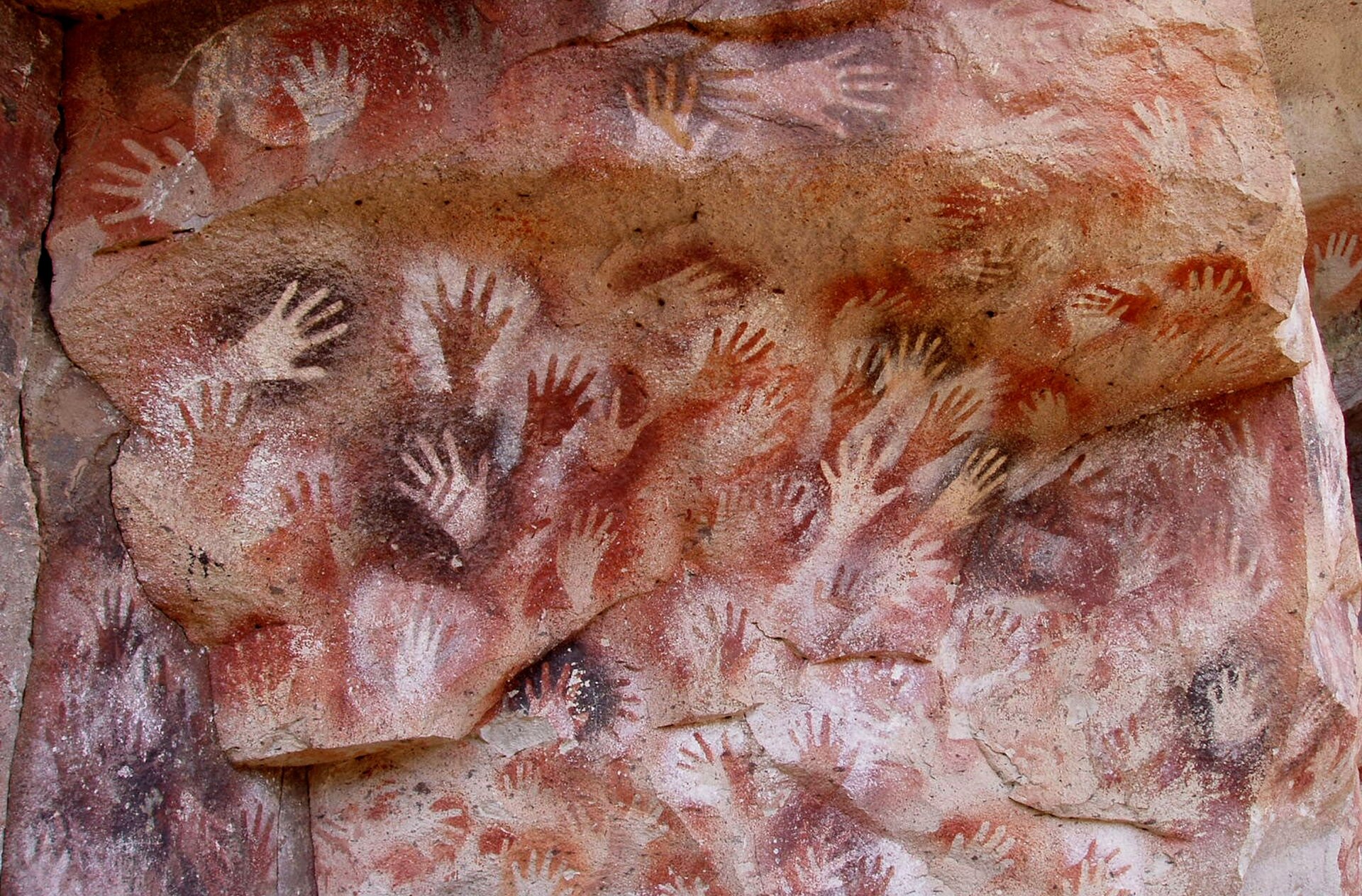 Zdjęcie przedstawia skałę, na której są namalowane ludzkie dłonie.