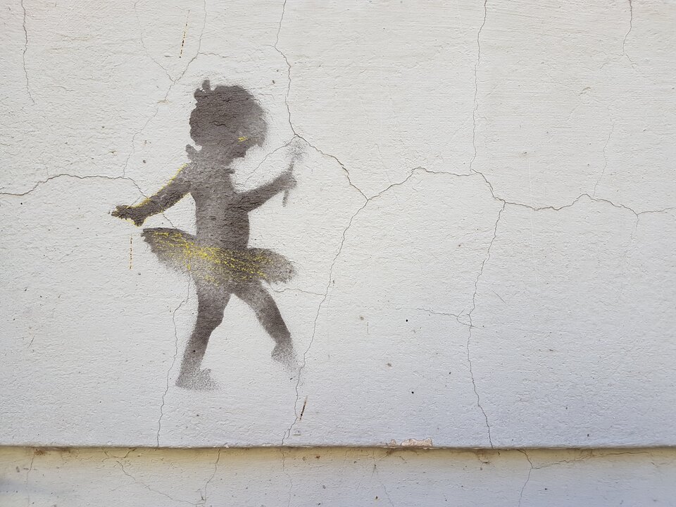 Ilustracja przedstawia graffiti na ścianie. Na fotografii znajduje się rysunek małej baletnicy, która w ręku trzyma różdżkę.