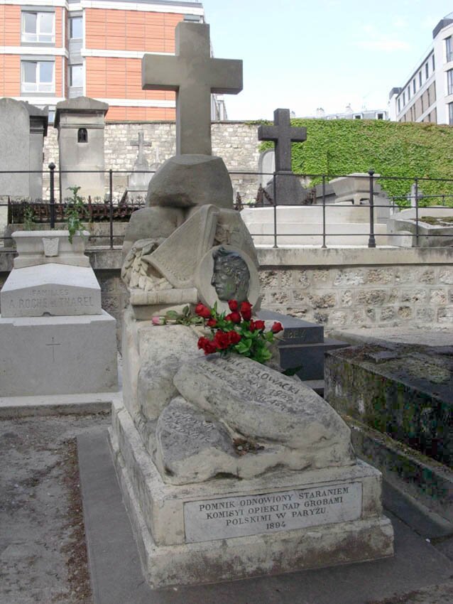 Zdjęcie przedstawia pomnik na cmentarzu. Pomnik zrobiony jest z krzyża górującego nad wezgłowiem grobu. Poniżej krzyża widoczna jest płaskorzeźba przedstawiająca lewy profil Juliusza Słowackiego. Nagrobek składa się z szeregu leżących na sobie głazów wyrzeźbionych w kamieniu. W nogach pomnika widnieje napis: Pomnik odnowiony staraniem Komisyi Opieki nad Grobami Polskimi w Paryżu 1804.