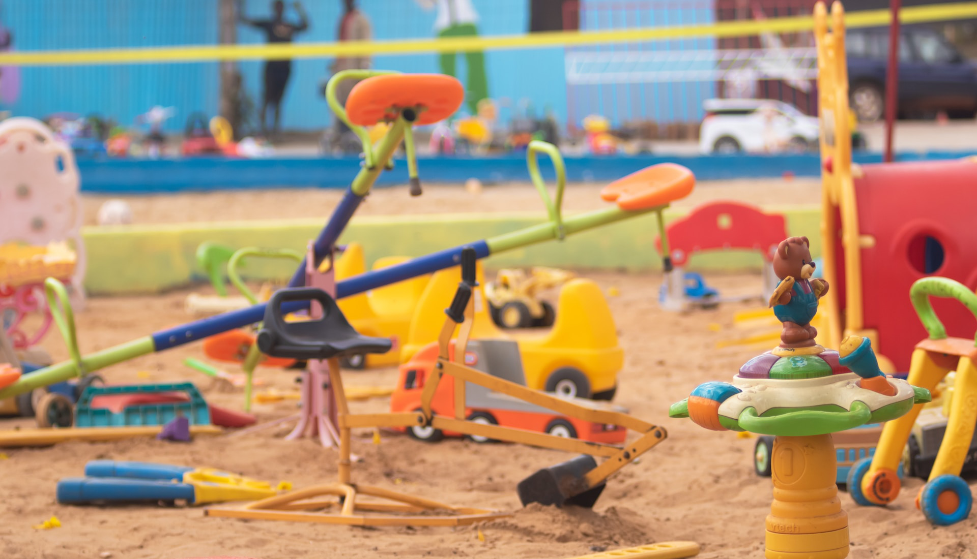 Zdjęcie przedstawia plac zabaw, na którym widoczne są huśtawki, piaskownica i zabawki pozostawione przez dzieci. 