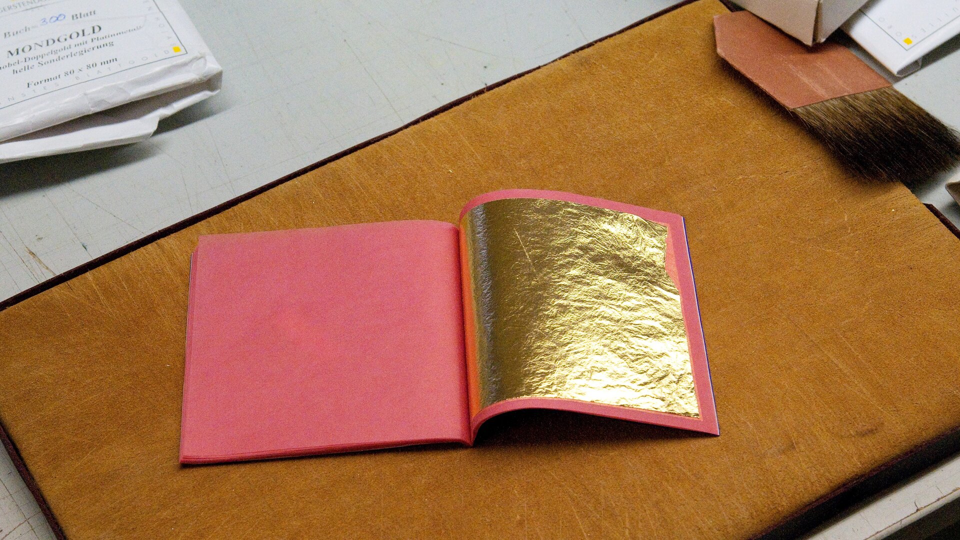 Zdjęcie przedstawia różowy zeszyt, na którym położono kawałek złotej folii.