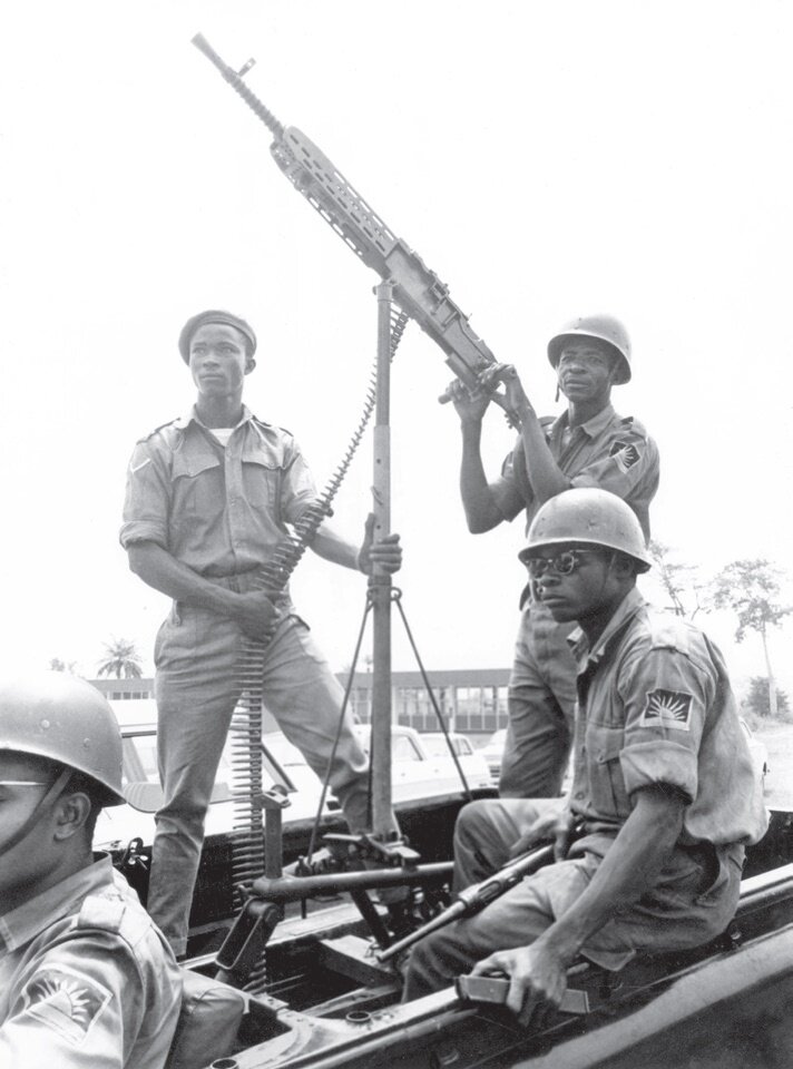 Na czarno‑białej fotografii znajdują się czarnoskórzy żołnierze w mundurach. Siedzą i stoją oni na wojskowym pojeździe z zamontowanym karabinem maszynowym. W tle widoczne są palmy i zabudowania.  