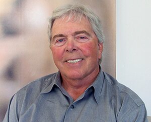 Fotografia przedstawia Herberta Boyera. Ma on siwe włosy i jest ubrany w szarą koszulę. Uśmiecha się do zdjęcia.