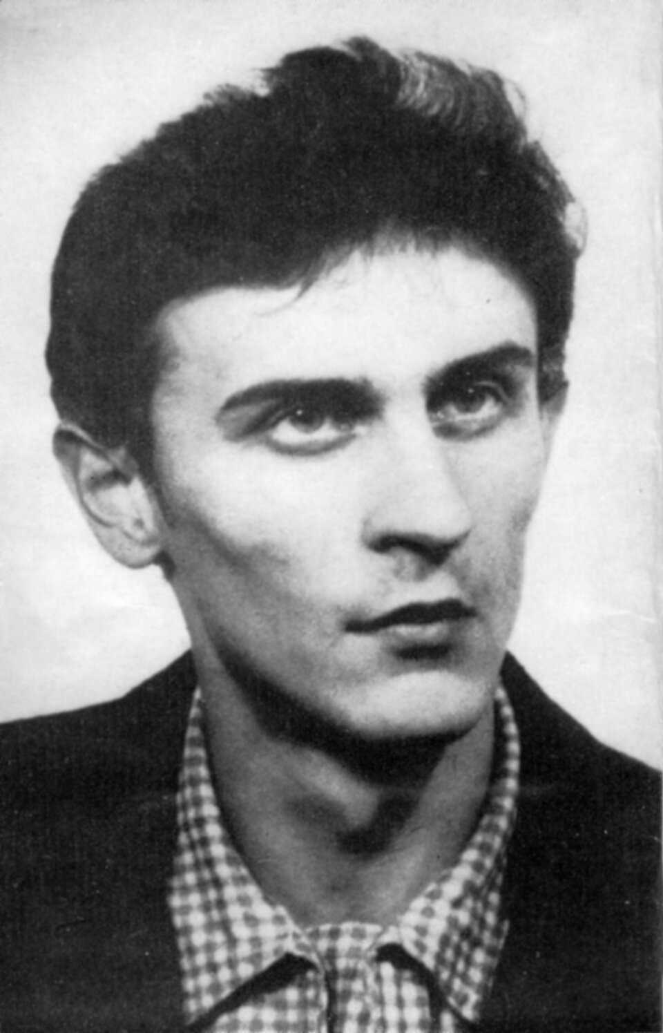 Zdjęcie przedstawia młodego mężczyznę. Ma szczupłą, pociągłą twarz i wyraźnie zaznaczone kości policzkowe. Mężczyzna ma głęboko osadzone oczy i wydatny nos. Jego ciemne włosy są krótko ostrzyżone.