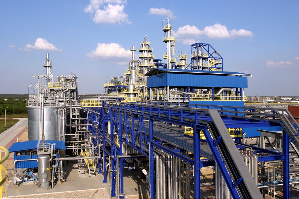 Zdjęcie przedstawiające fragment zabudowań Zakładów Azotowych w Puławach. Większość budynków to metalowe konstrukcje pokryte niebieską farbą lub pozostawione w oryginalnym metalicznym połysku. W tle znajduje się droga oraz lasy. Nad zakładami błękitne niebo z niedużą ilością białych chmur.