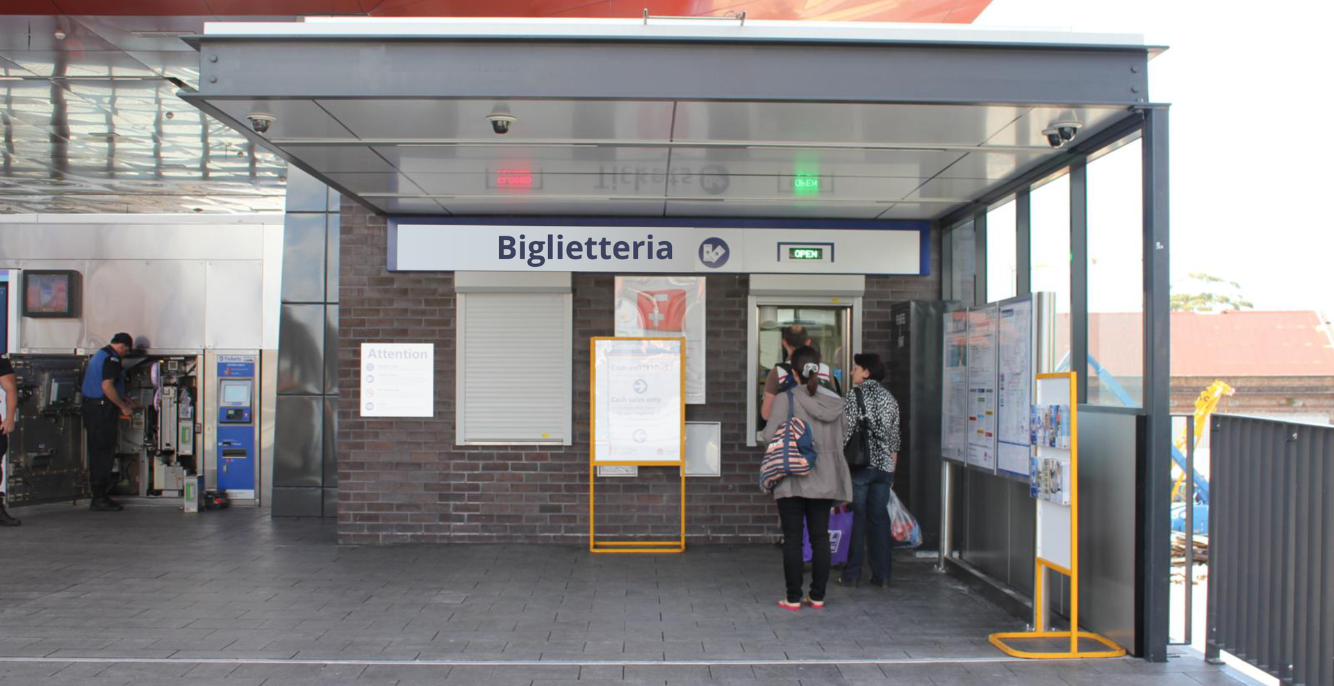 Zdjęcie przedstawia kasę biletową na dworcu kolejowym. Przed kasą stoi kilka osób.