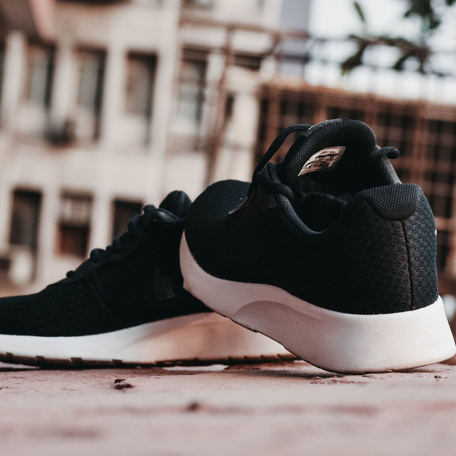 Ilustracja przedstawia czarne buty z wysoką białą podeszwą. Jeden but,opiera się o drugi. W tle widoczne są budynki.