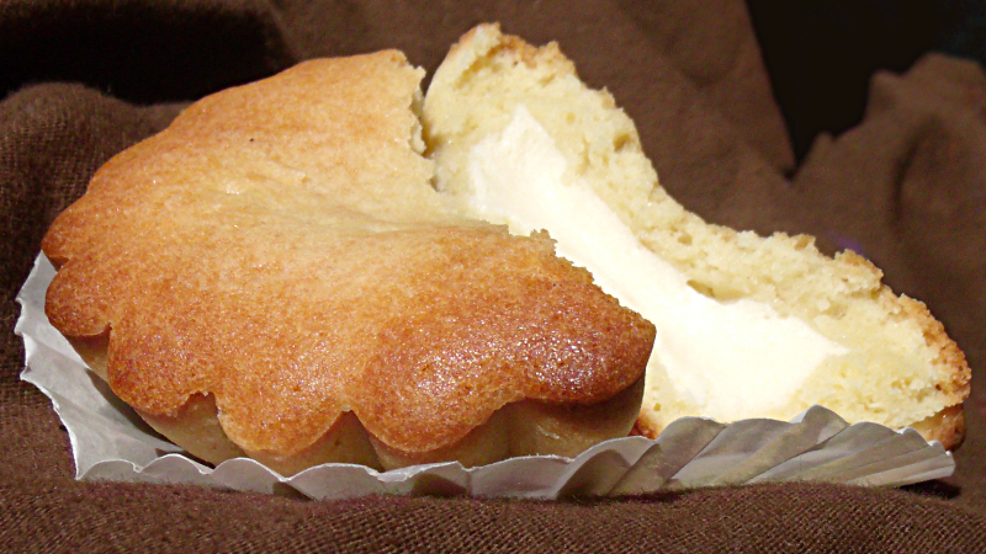 Na zdjęciu pokazana jest krucha babeczka Pasticciotto, która została przełamana. Widoczne jest kremowe nadzienie ciastka.