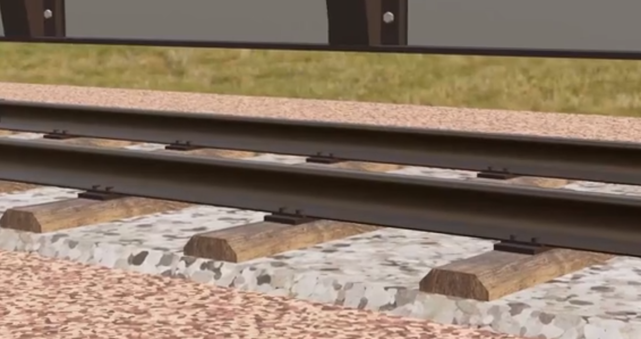 Ilustracja przedstawia tor kolejowy. Widoczne są szyny osadzone na podkładach ustawionych na podsypce. Powyżej widoczny jest przejeżdżający po torze wagon towarowy.