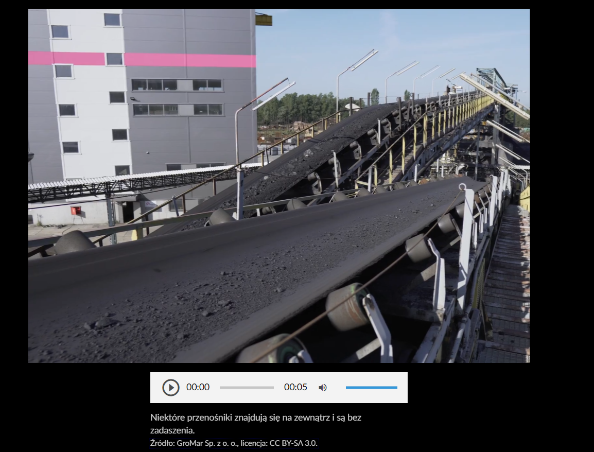 Na zdjęciu widoczna jest przykładowa grafika galerii zdjęć. W centralnej częśći zdjęcia widoczne są dwa taśmociągi którymi transportowany jest węgiel. Za taśmociągami znajduje się budynek wielkokubaturowy budynek przemysłowy.  W budynku znajdują się okna.Poniżej grafiki znajduje się panel multimedialny. Kolejne ikony na panelu: trójkąt w kole, cyfry pokazujący czas początkowy, belka pokazująca postęp nagrania, cyfry pokazujące koniec nagrania, głośnik, belka pokazująca poziom głośności.Pod panelem multimedialnym widoczny jest napis: Niektóre przenośniki znajdują się na zewnątrz i są bez zadaszenia. 