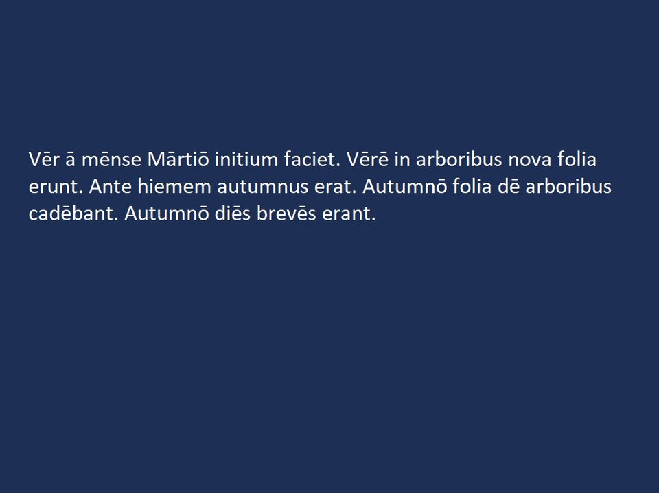 Plansza z białym napisem na ciemnoniebieskim tle:
„Vēr ā mēnse Mārtiō initium faciet. Vērē in arboribus nova folia erunt. Ante hiemem autumnus erat. Autumnō folia dē arboribus cadēbant. Autumnō diēs brevēs erant.”