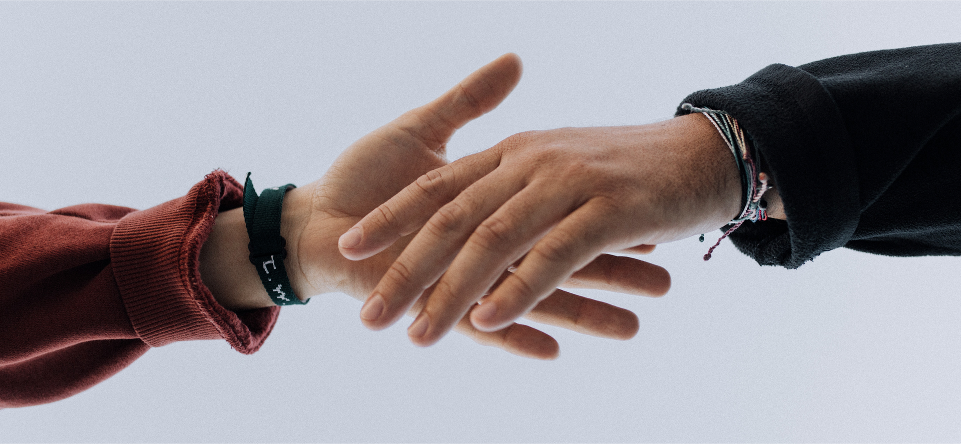 Zdjęcie przedstawia dwie dłonie różnych osób. Dłonie wyciągnięte są ku sobie w geście pomocy. Po prawej stronie widoczna jest męska dłoń, po lewej dłoń młodej osoby. Na obu nadgarstkach widoczne są bransoletki.
