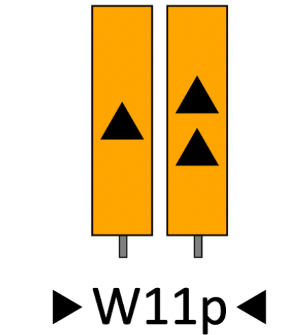 Wskaźnik wu jedenaście pe. To dwa długie żółte prostokąty o dłuższym pionowym boku. mają te same wymiary i są osadzone na słupku każdy. Na każdym z nich pośrodku znajdują się czarne trójkąty równoboczne. Na lewym jeden trójkąt, na prawym dwa trójkąty jeden pod drugim.