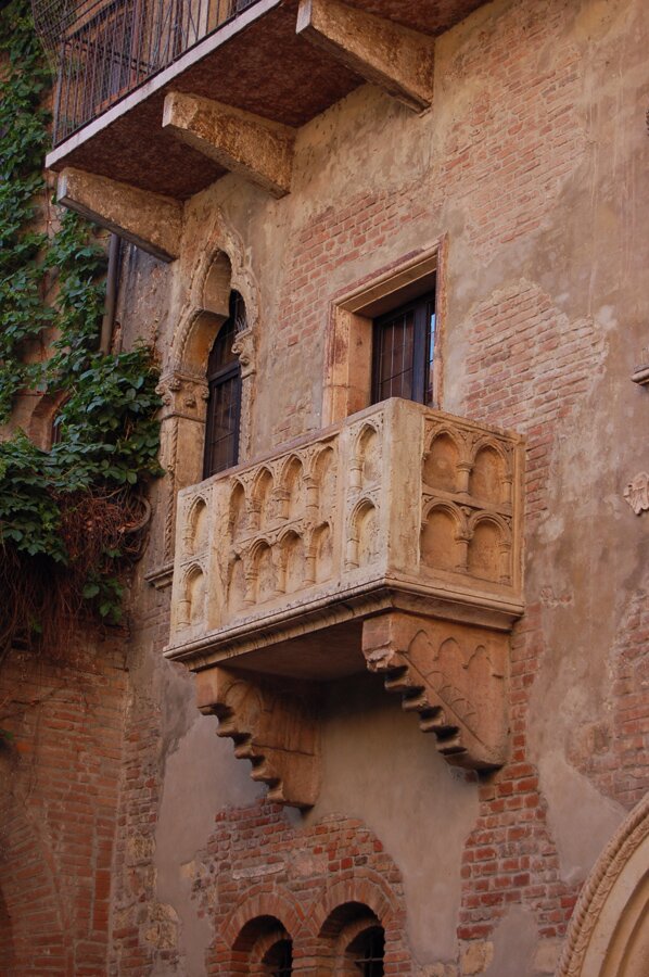 Zdjęcie przedstawia dom z cegły. Na jego zewnętrznej ścianie widoczny jest niewielki balkon.