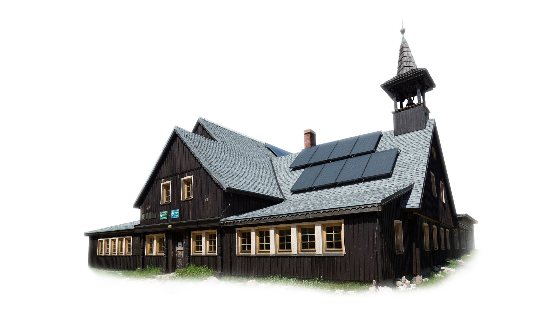 Zdjęcie przestawia duże przestronne schronisko o ciemnobrązowych ścianach z szarym spiczastym dachem. W jednym miejscu wyrasta z niego niska wieża z dzwonnicą. Na dachu zamontowane są panele słoneczne. Budynek jest w stanie pomieścić kilka grup ludzi.