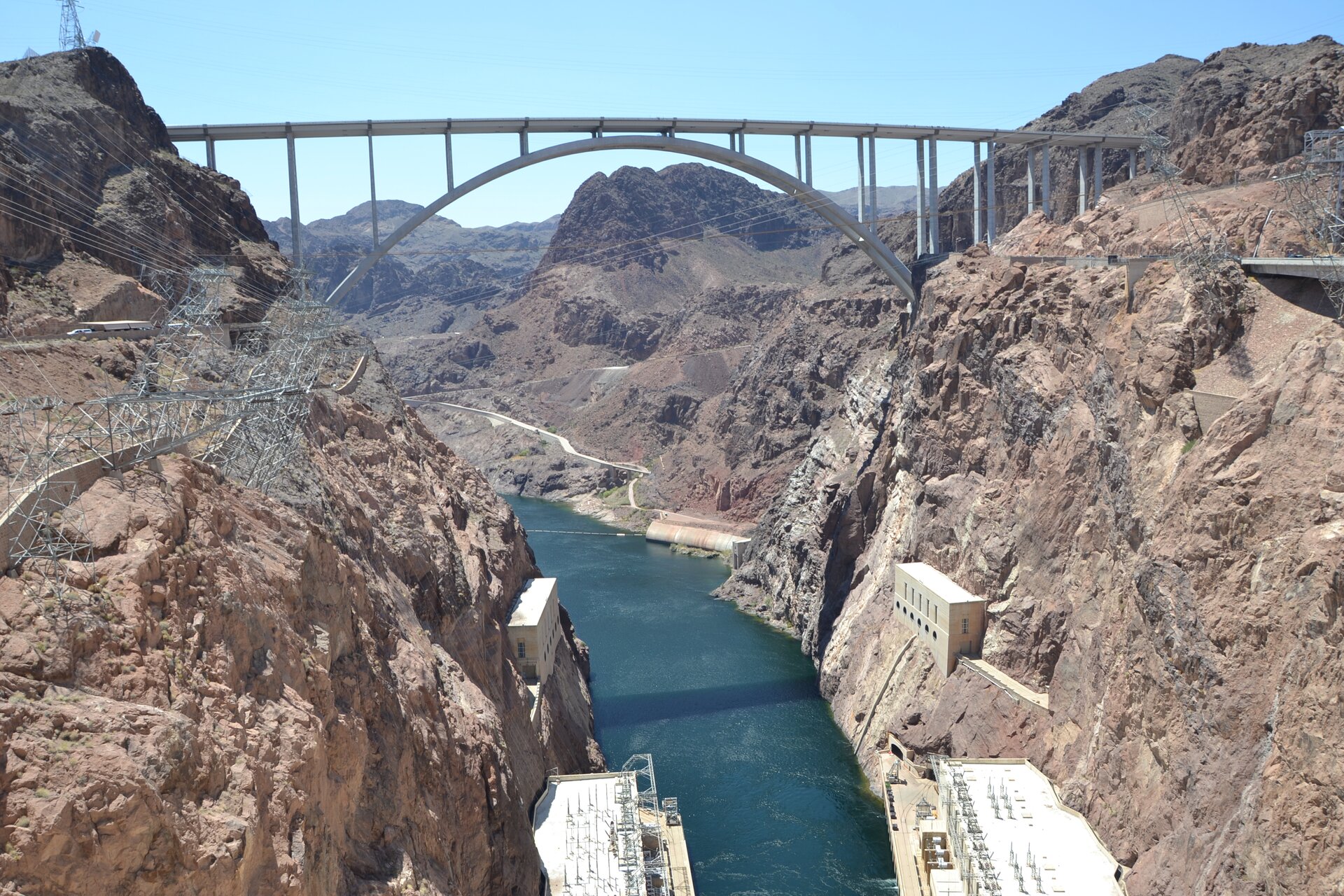 Zdjęcie przedstawia most łączący dwa skaliste brzegi rzeki koło Zapory  Hoovera w USA. Konstrukcja mostu opiera się na łuku, który za pomocą stalowych pionowych podpór podtrzymuje poziomą część, którą biegnie droga. W dole płynie rzeka, na brzegu której przy skalistych brzegach zostały wybudowane obiekty o bryłach przypominających małe pudełka.