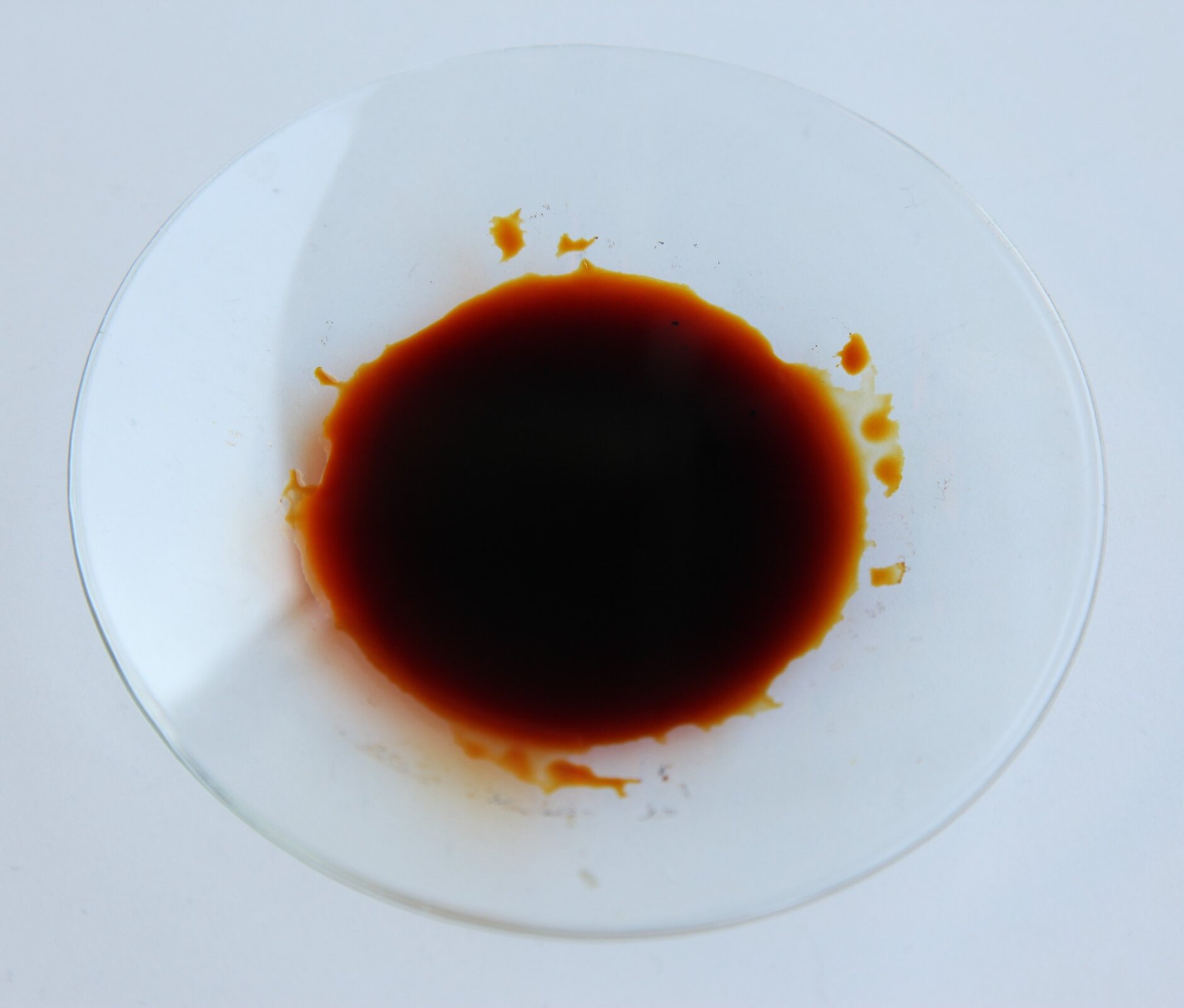 Na zdjęciu widać przezroczysty okrągły talerzyk na stole. W środku znajduje się płyn koloru czerwono‑brązowego.