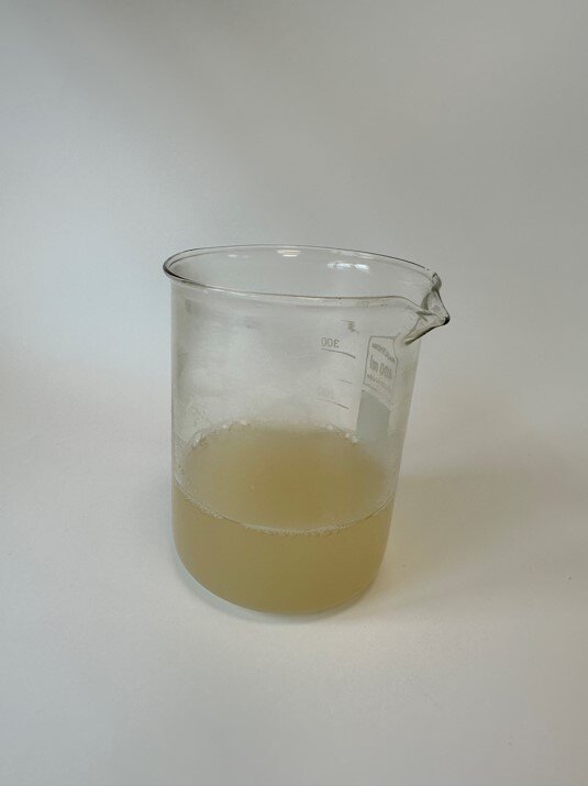 Zdjęcie przedstawia szklane naczynie z brunatną cieczą - roztworem skrobi.
