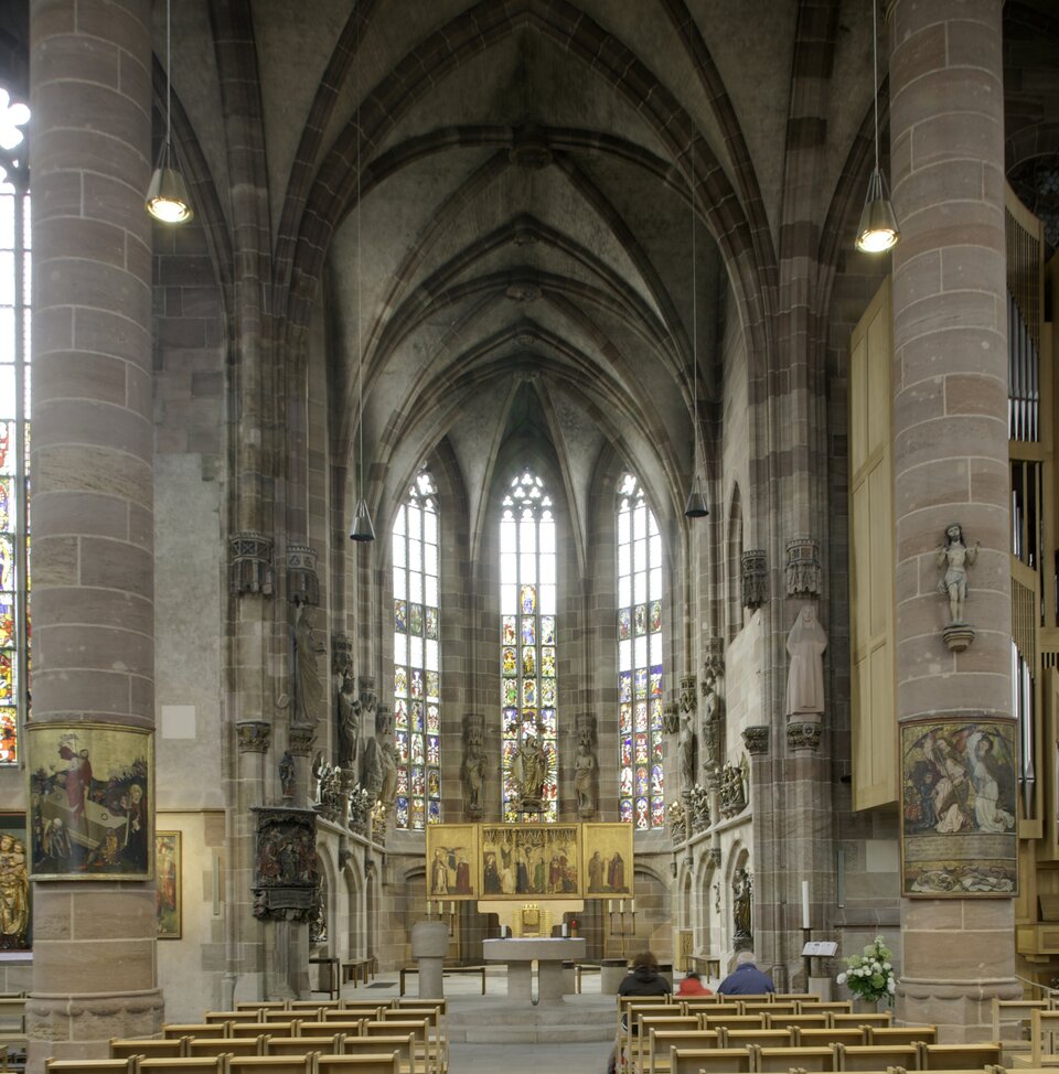 Wnętrze kościoła Najświętszej Maryi Panny w Norymberdze. Widok nawy głównej, na dalszym planie ołtarz, za nim trzy wysokie i wąskie okna z witrażami. 