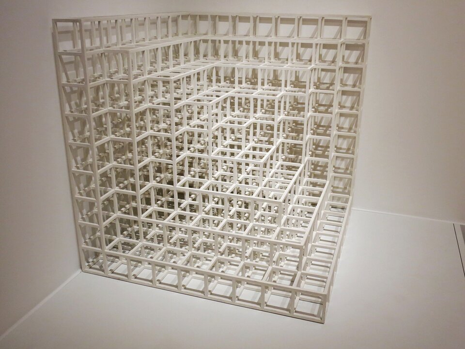 Fotografia przedstawia rzeźbę „Floor‑Corner 2” autorstwa Sol LeWitta. Praca ta, to modułowo połączone ze sobą białe sześciany, które są ułożone piętrowo – cała rzeźba składa się z dziewięciu warstw. Rzeźba ta znajduje się obok narożnika ściany. 