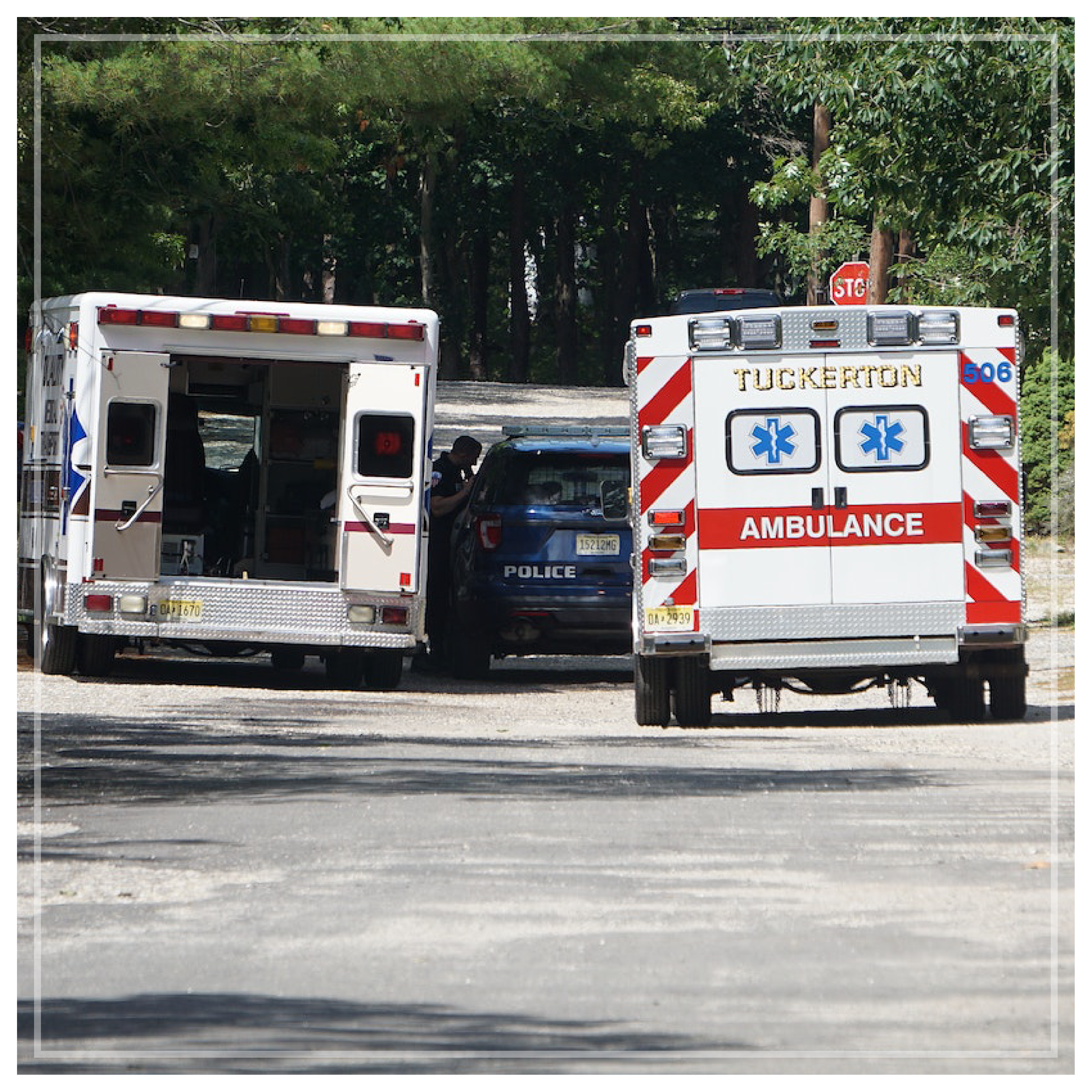 Na zdjęciu znajdują się dwa zaparkowane ambulanse, a między nimi wóz policyjny. Jeden z ambulansów ma otwarte tylne drzwi. 