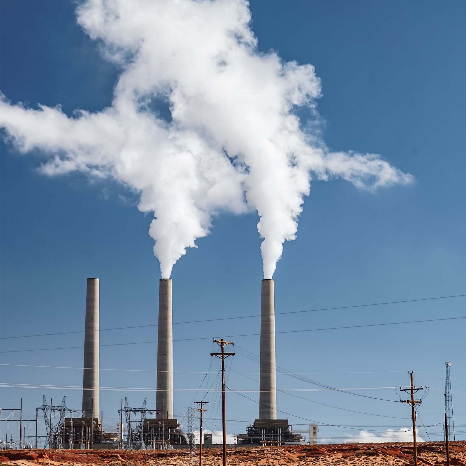 Zdjecie przedstawia trzy wysokie, wysmukłe kominy, z których wydobywa się dym. 