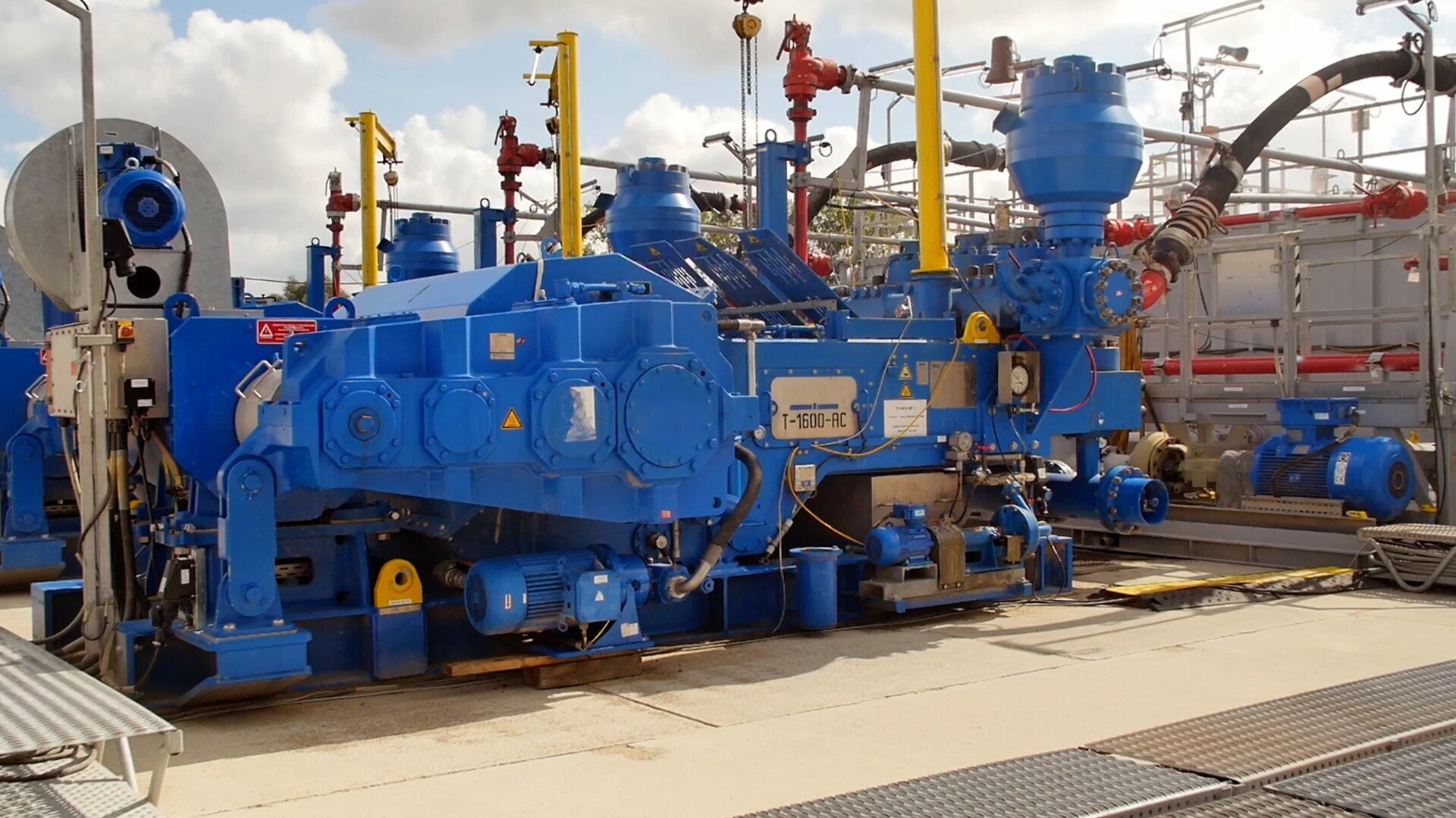 Zdjęcie przedstawia pompę płuczkową czyli odpowiadające za zatłaczanie płuczki wiertniczej na dno otworu z odpowiednio wysokim ciśnieniem pozwalającym na pokonanie oporów przepływu i wyniesienie płuczki z fazą stałą (zwiercinami) na powierzchnię. Pompa płuczkowa jest podłużnym urządzeniem, wykonanym ze stali pomalowanej na kolor niebieski. Do końcówki urządzeina przymocowany jest, gruby elastyczny wąż, który podłączony jest do czerwoego rurociągu. Na zdjęciu widnieje silnik elektryczny napędzający pompę płuczkową, pompa płuczkowa typu triplex wykorzystywana podczas wierceń normalnośrednicowych z prawym obiegiem płuczki wiertniczej. Konstrukcja pompy przewiduje możliwość zamontowania tulei cylindrowych różnych średnic, do pozwala na regulację maksymalnego ciśnienia tłoczenia. Wraz ze wzrostem średnic tulei cylindrowych maksymalne ciśnienie tłoczenia maleje, a strumień objętości rośnie. Strumień objętości pompy jest regulowany również przez zmianę prędkości obrotowej silnika napędzającego pompę oraz odśrodkowa pompa doładowująca ssąco‑tłocząca.