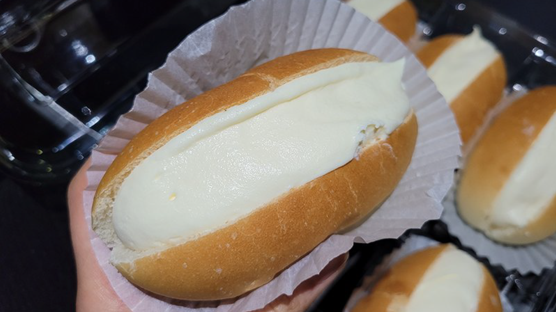 Zdjęcie przedstawia kilka drożdżowych, podłużnych bułeczek, które zostały nacięte i wypełnione bitą śmietaną. Jest to włoski deser Maritozzo con la panna.