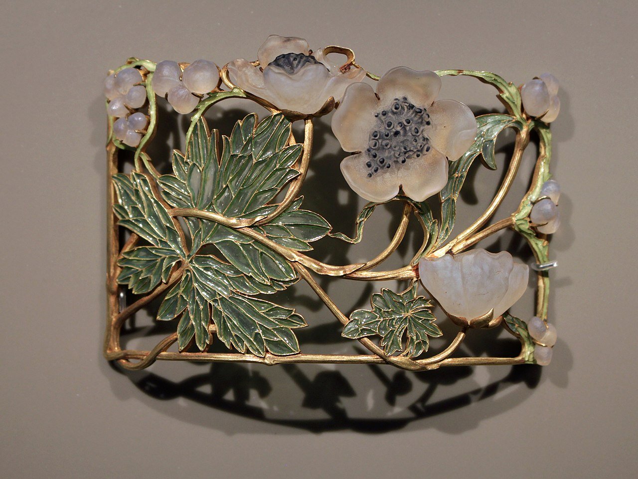 Zdjęcie przedstawia secesyjną broszkę zrobioną ze złota i kamieni. Znajduje się na niej motyw kwiatowy.