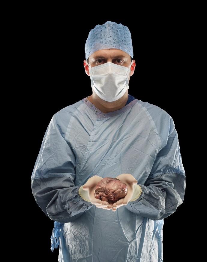 Zdjęcie przedstawia mężczyznę w fartuchu, z czepkiem na głowie i maską na twarzy. Przed sobą w rękach trzeba jasnoróżowe serce.