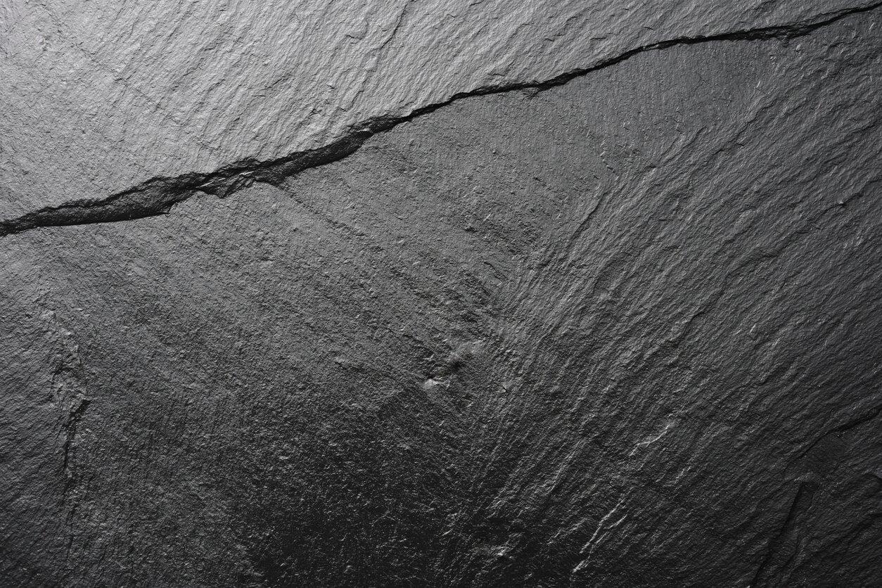 Na zdjęciu znajduje się gładka faktura bazaltu, przez którego powierzchnię przechodzi pęknięcie. Kamień ma barwę grafitu wpadającego w czerń.