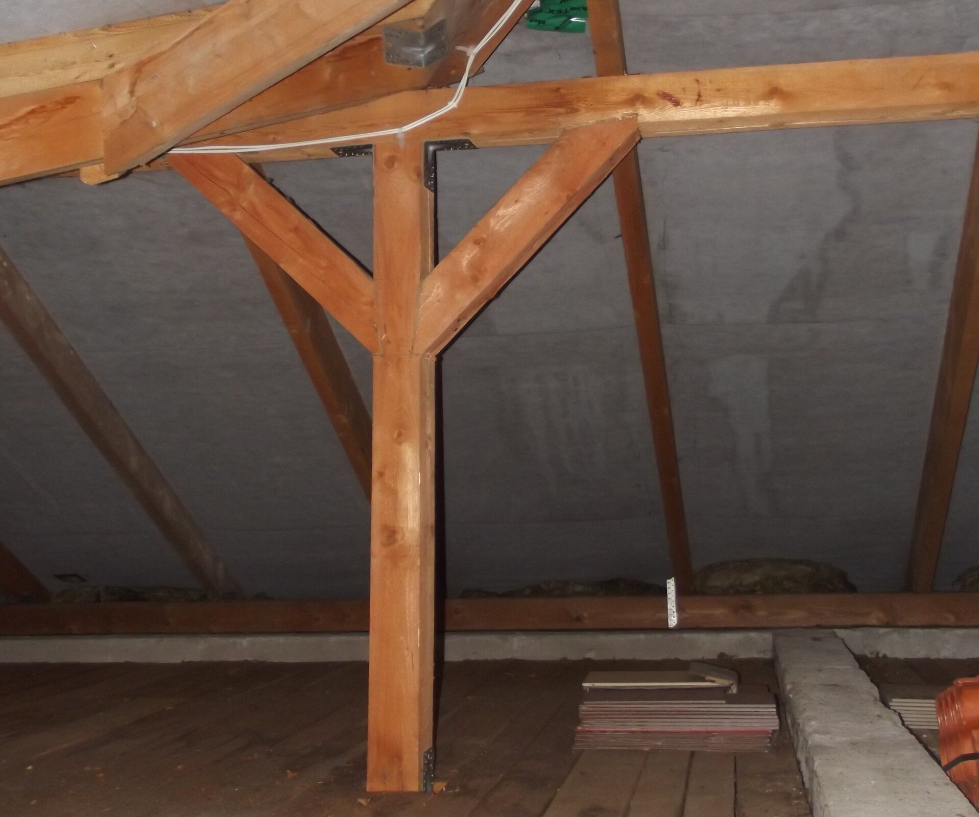 Rys. a. Zdjęcie przedstawia drewniany strop budynku. Dach budynku oparty jest na drewnianej konstrukcji więźby dachowej, na pierwszym planie pokazano słup i krokwie wykonane z drewnianych belek. Są to elementy konstrukcji podtrzymujące dach. Deski oraz belki, z których wykonana jest konstrukcja dachu poprzebijane są gwoździami. Pomiędzy drewnianymi elementami, które stykają się wzajemnie, występuje również siła tarcia. Siła tarcia pomiędzy elementami oraz przybicie elementów gwoździami zapewnia stabilność konstrukcji.