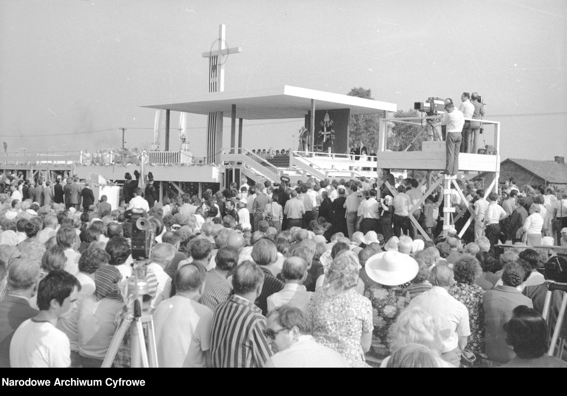 Zdjęcie przedstawia wielotysięczny tłum zebrany wokół podwyższenia, na którym usytuowany jest ołtarz. Monumentalny stojący krzyż góruje nad całym placem.