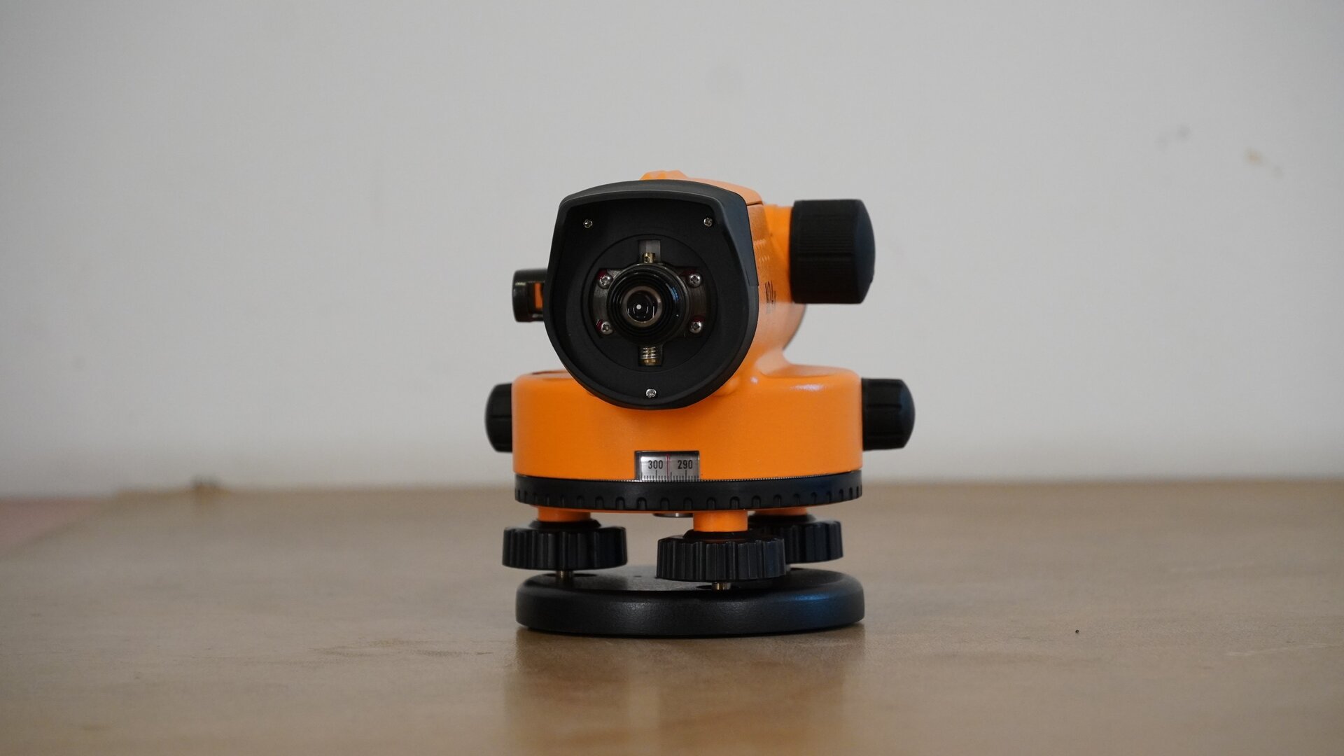 Zdjęcie ukazuje niwelator od strony okularu, z którego odkręcono obudowę. Po lewej jego stronie widoczne jest lusterko libelli, a poniżej korpus z dwoma pokrętłami po bokach oraz podziałką koła poziomego poniżej. Pod kołem poziomym znajdują się trzy śruby umieszczone na okrągłej podstawie, czyli spodarce.