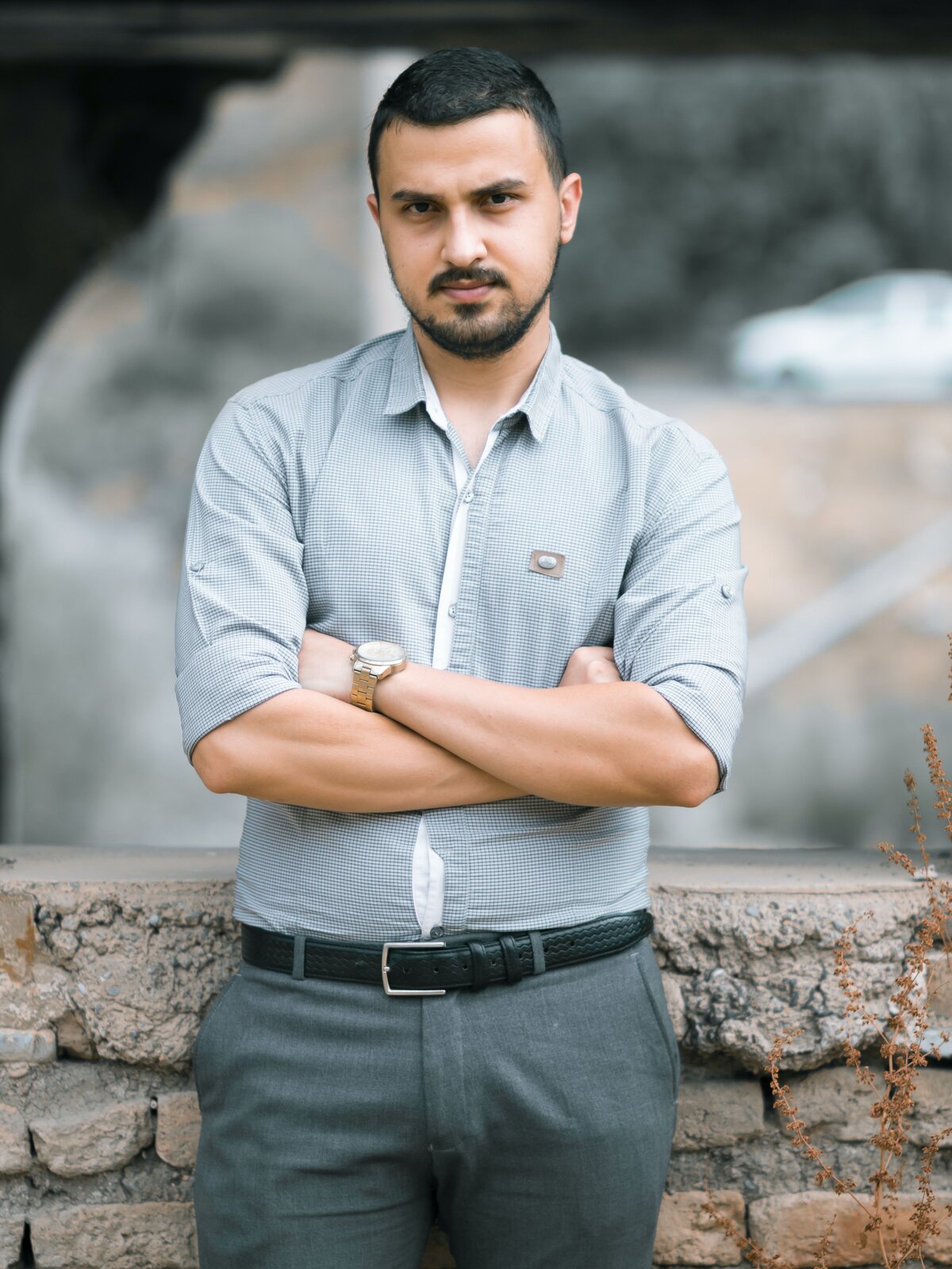 Zdjęcie przedstawia młodego mężczyznę ubranego w jasno niebieską koszulę, szare spodnie, do których założył czarny pasek. 