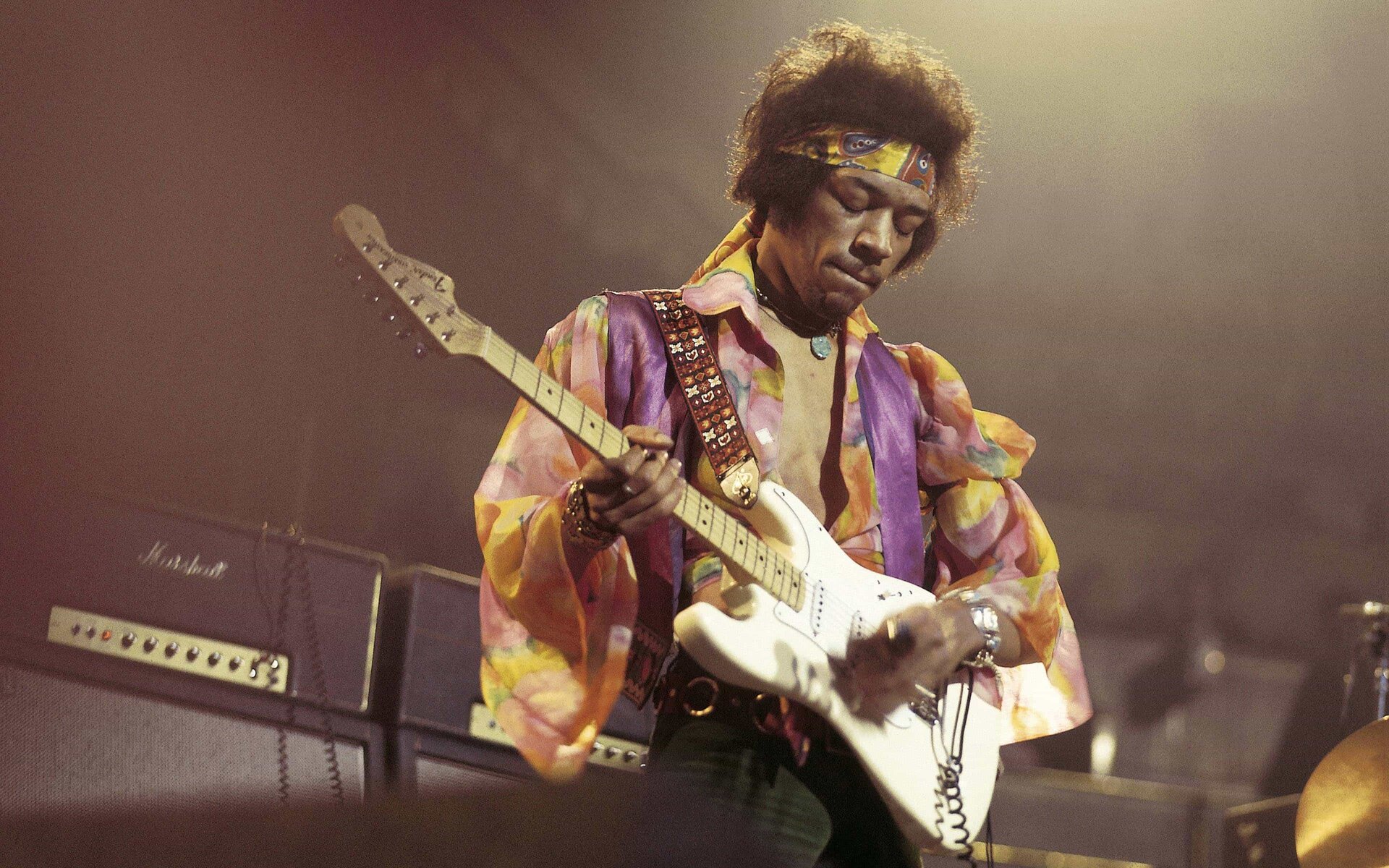 Ilustracja przedstawia amerykańskiego gitarzystę, wokalistę, kompozytora oraz autora tekstów Jimiego Hendrixa. Mężczyzna znajduje się na scenie podczas koncertu. Gra na gitarze. Ubrany jest w kolorową koszulę.