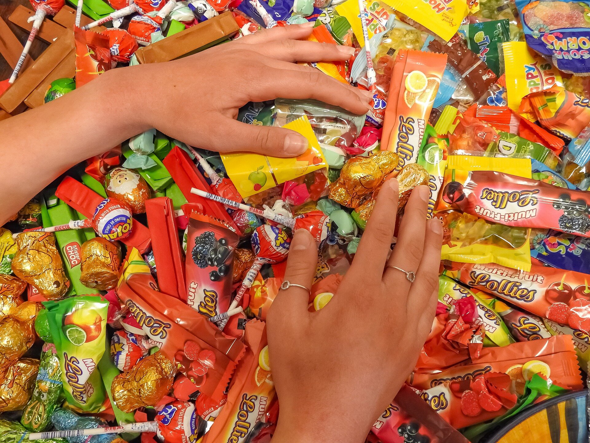 Zdjęcie przedstawia kobiece dłonie leżące na stosie cukierków, batoników i lizaków.