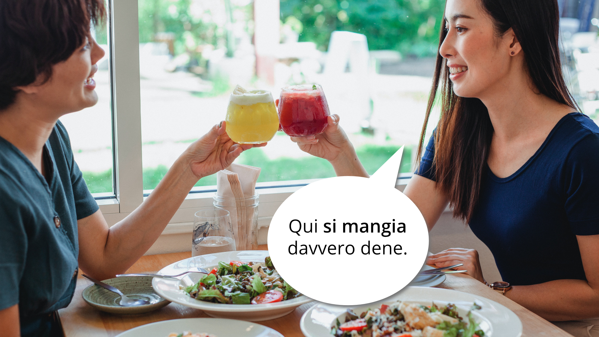 Zdjęcie przedstawia dwie kobiety siedzące naprzeciwko siebie przy stoliku w restauracji. Kobiety trzymają w ręku szklanki z napojami. Na stoliku przed nimi stoją talerze z sałatkami. Obok jednej z kobiet znajduje się dymek z tekstem: Qui si mangia davvero bene.