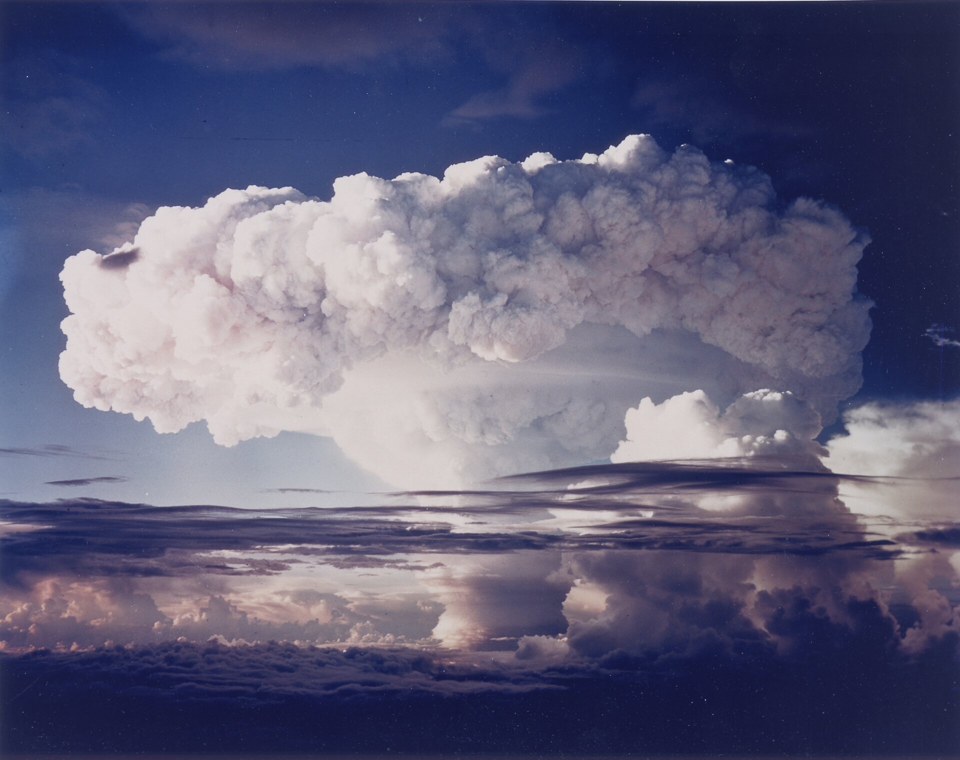 Kolorowe zdjęcie 6: Ivy Mike, próba jądrowa nad oceanem. Zdjęcie przedstawia białą chmurę tworzącą grzyb atomowy. Górna część grzyba to kłęby białych chmur ułożonych w krąg.
